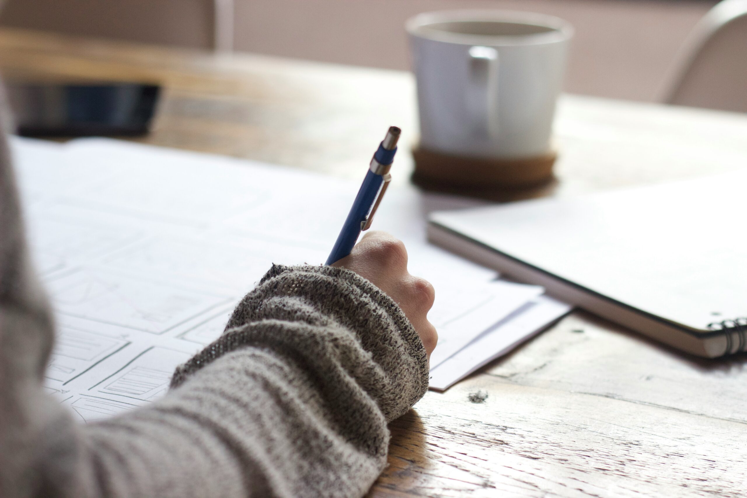person writing on brown person writing on brown wooden table near white ceramic mug